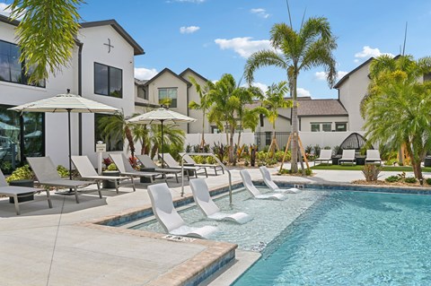 A pool with chairs and umbrellas in front of a building. at The Hadley - North Port, FL Apartments, North Port, Florida