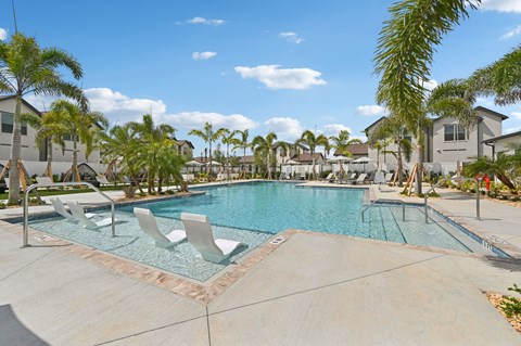 A swimming pool surrounded by palm trees and lounge chairs.