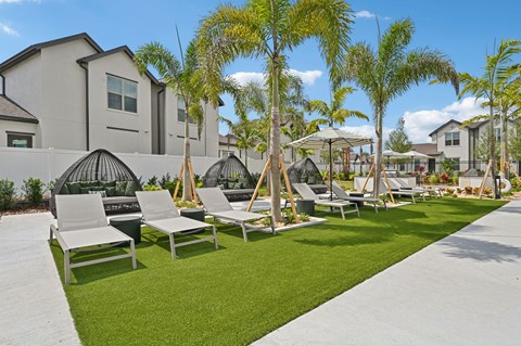 A row of white lounge chairs are set up on a lawn at The Hadley - North Port, FL Apartments, Florida