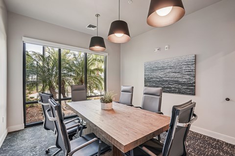 A conference room with a long table and chairs, a plant, and a painting on the wall.