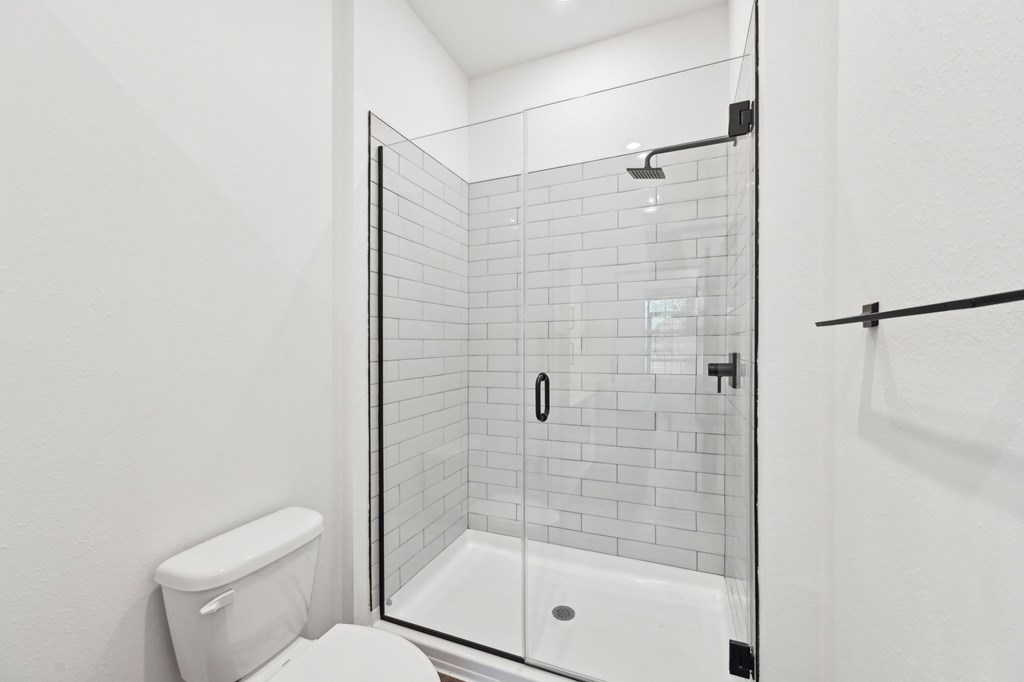 A white toilet sits next to a walk-in shower with a glass door at The Concord Luxury Apartments, Sarasota 34240