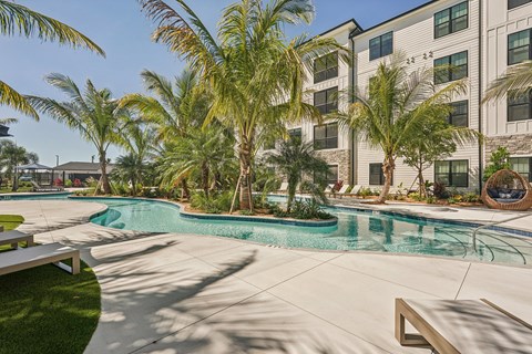 A pool surrounded by palm trees and a building in the background.