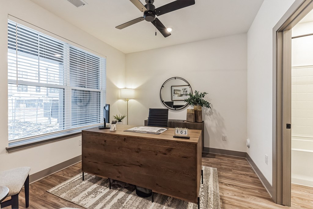 an office with a large window and a wooden desk and a ceiling fan at Meridian at CityPlace, Woodbury, MN