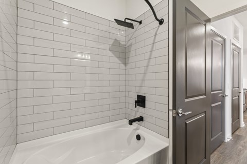 A white bathtub in a bathroom with a grey door. at The Junction at Rockledge Apartments, Rockledge 32955