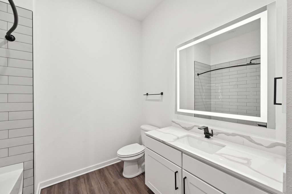 A white bathroom with a toilet, sink, and mirror at The Concord Luxury Apartments, Sarasota