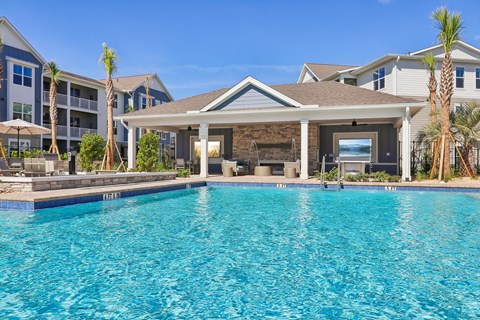 A swimming pool in front of a house with a patio and palm trees.