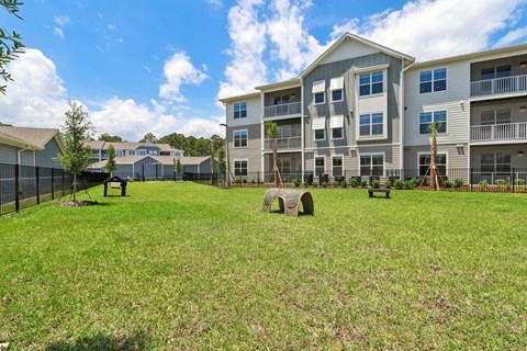 A grassy area in front of apartment buildings with a fence and benches.