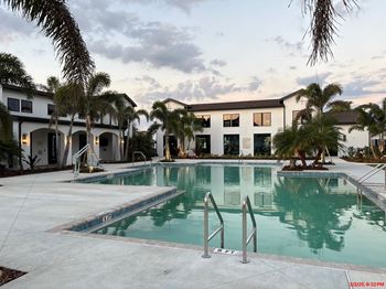A swimming pool in front of a building with palm trees.