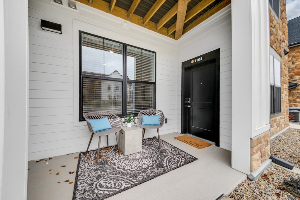 the front porch of a home with two chairs and a table and a black door at The BLVD at Wilson Crossings, Michigan