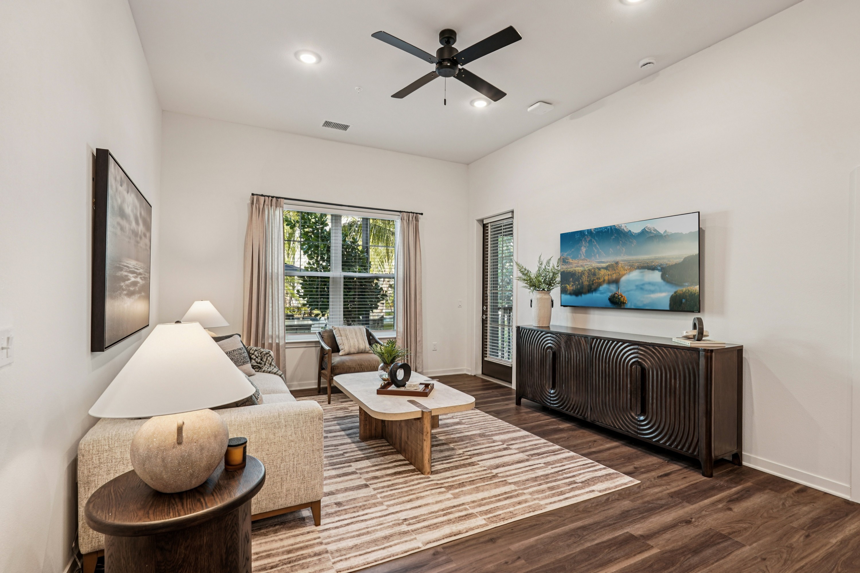 A living room with a ceiling fan and a painting of a lake.