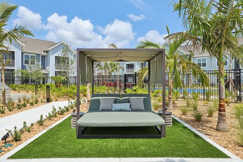 A green outdoor daybed with a canopy is situated in a landscaped yard. at The Junction at Rockledge Apartments, Rockledge, FL, 32955