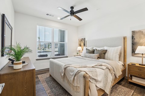 A bedroom with a large bed, a ceiling fan, and a window with blinds. at The Junction at Rockledge Apartments, Florida
