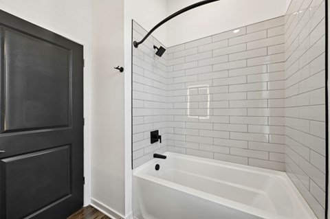 A white bathtub is in a bathroom with black tile at The Hadley - North Port, FL Apartments, North Port, FL