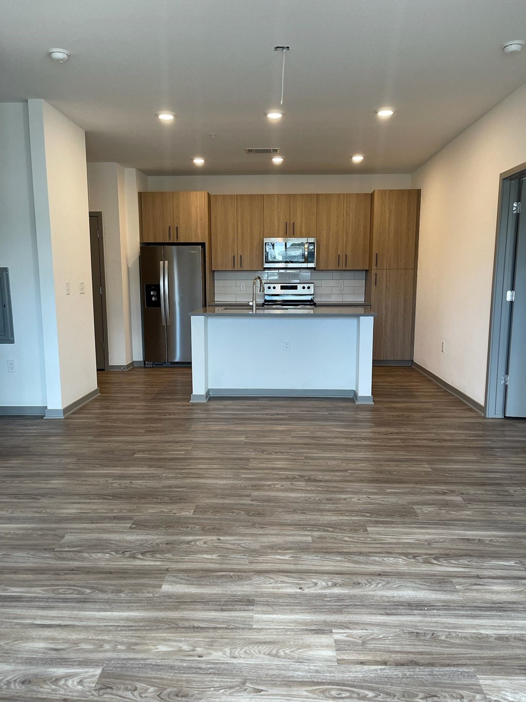 an empty living room with a kitchen and wood flooring