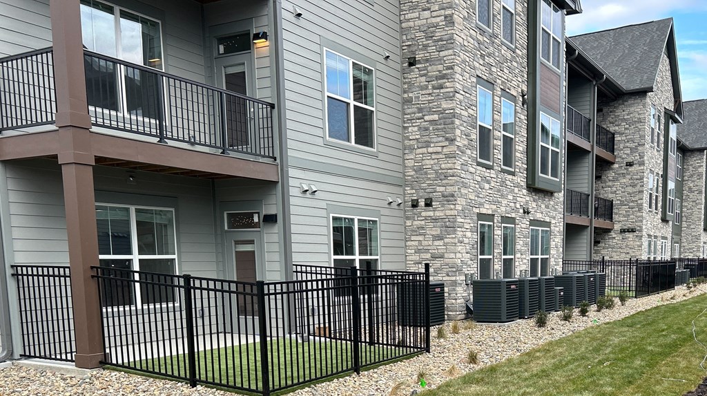an apartment building with a yard and a black fence at The Depot, Raymore, MO, 64083