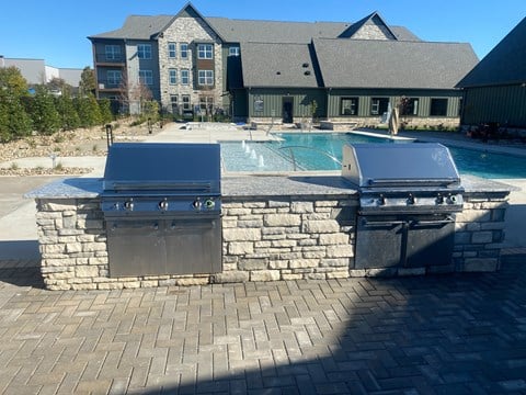 two stainless steel grills in front of a pool with a house in the background