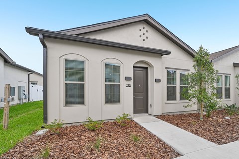 A small house with a brown door and a small tree in front at The Hadley - North Port, FL Apartments, North Port 34287
