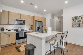 a kitchen with wooden cabinets and a large island with a sink and three stools at Apex, Colorado Springs, 80923