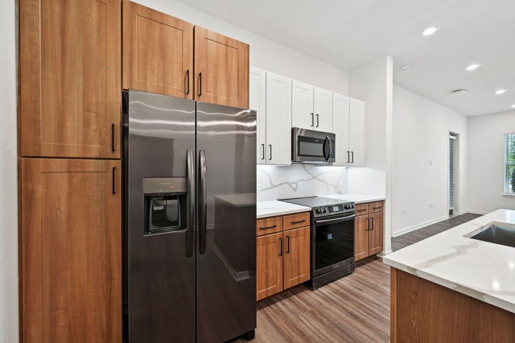 A modern kitchen with a stainless steel refrigerator and wooden cabinets at The Concord Luxury Apartments, Sarasota, FL
