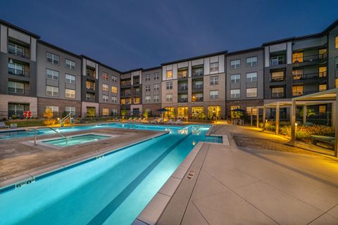 a swimming pool at night with an apartment building in the background