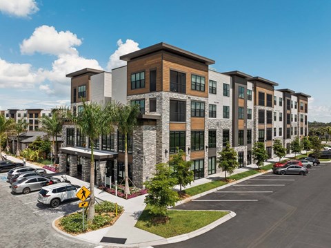 A row of modern apartment buildings with a parking lot in front.