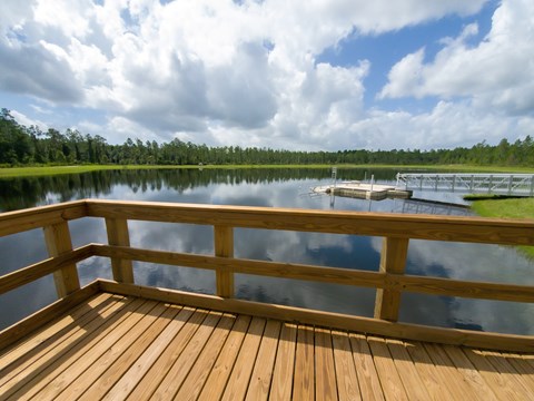 A wooden deck overlooks a calm lake with a dock and trees in the distance at Velara Luxury Apartments, Florida, 32081
