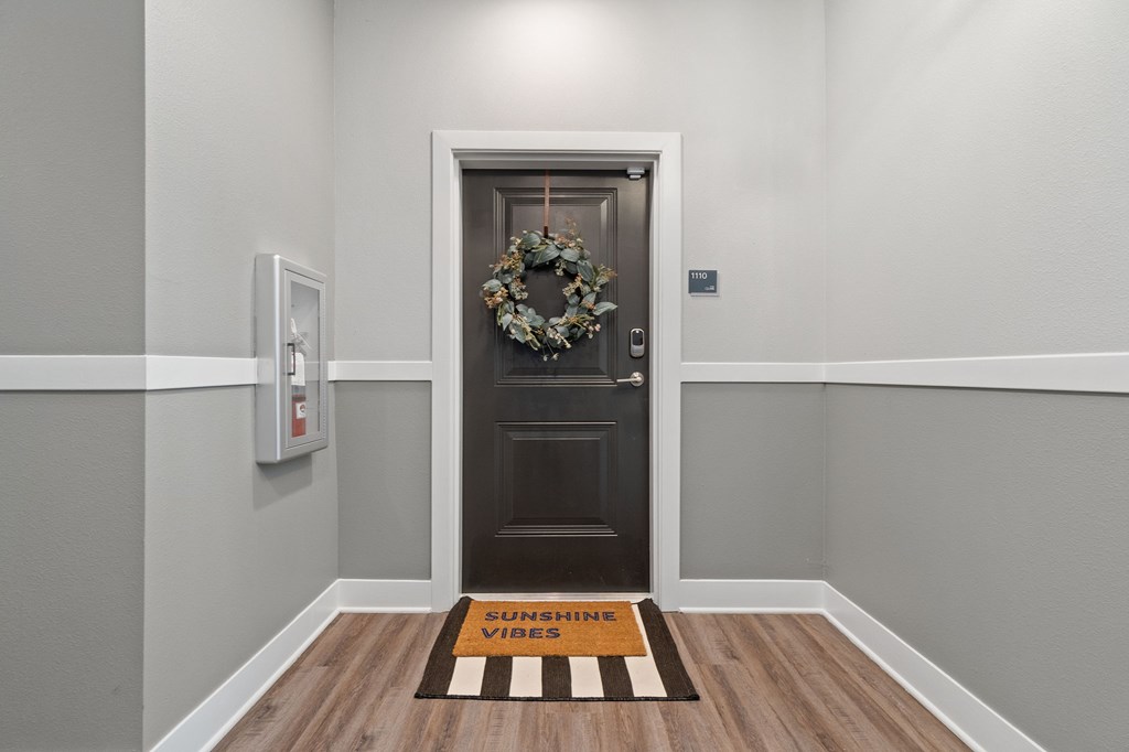 A door with a wreath on it and a mat on the floor.
