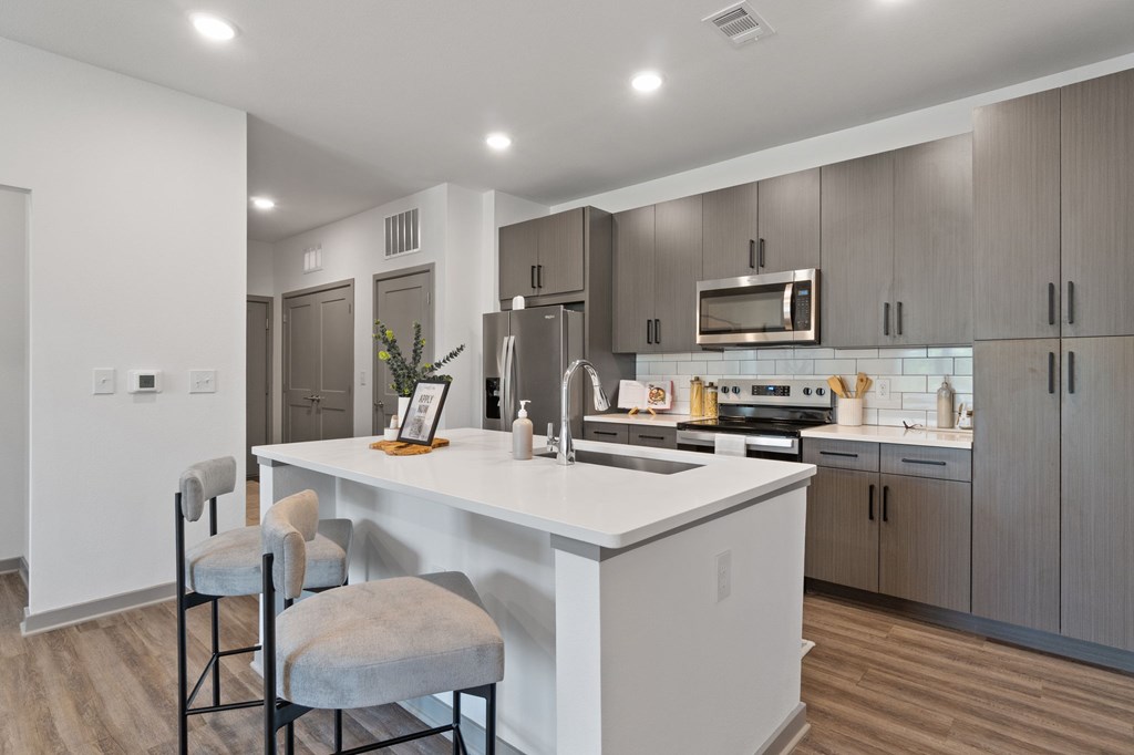 A modern kitchen with a white island and grey chairs.
