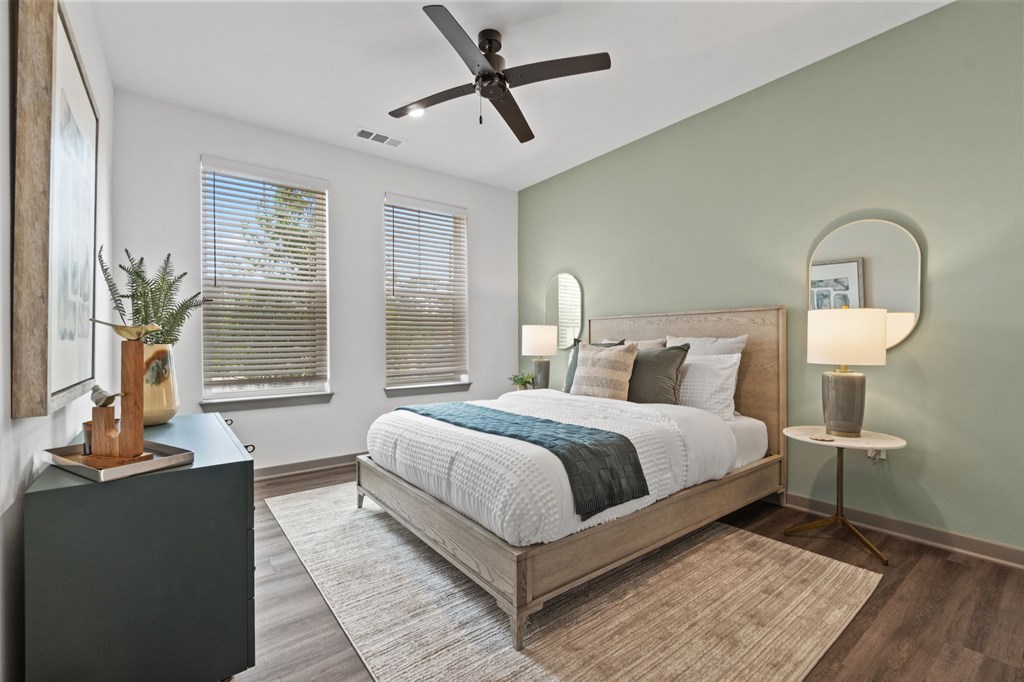 A bedroom with a bed, nightstand, and a plant on a table.