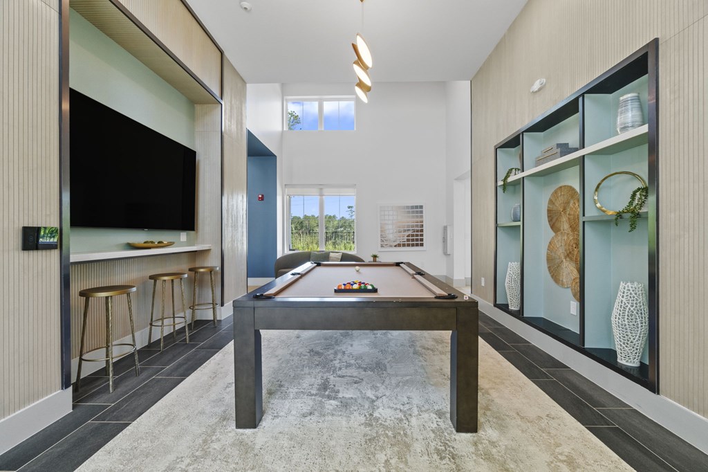 A billiard table is in the middle of a room with a television and bar stools.