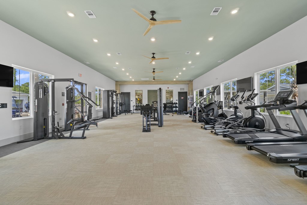 A spacious gym with treadmills, elliptical machines, and a fan.