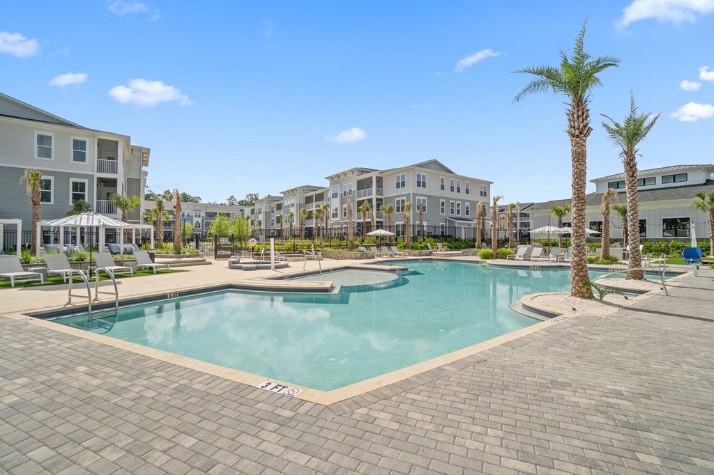 A large swimming pool surrounded by a brick patio and palm trees.