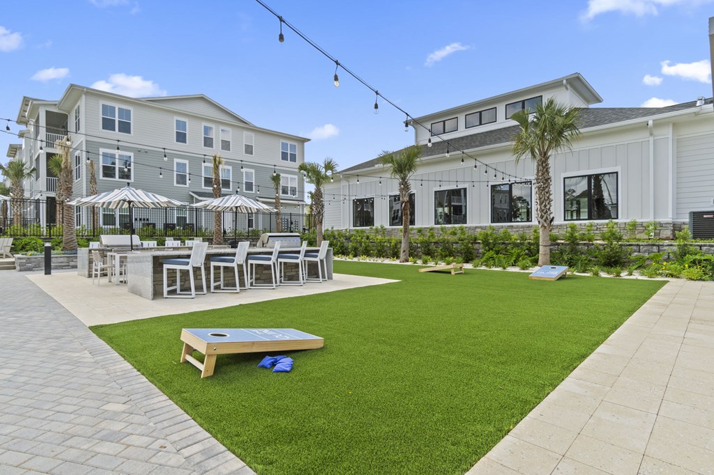 A patio area with a table and chairs is surrounded by a grassy area and a building in the background.