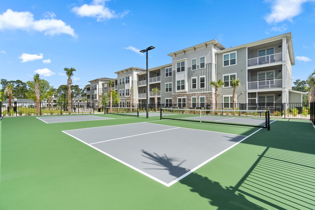 A tennis court is surrounded by apartment buildings.