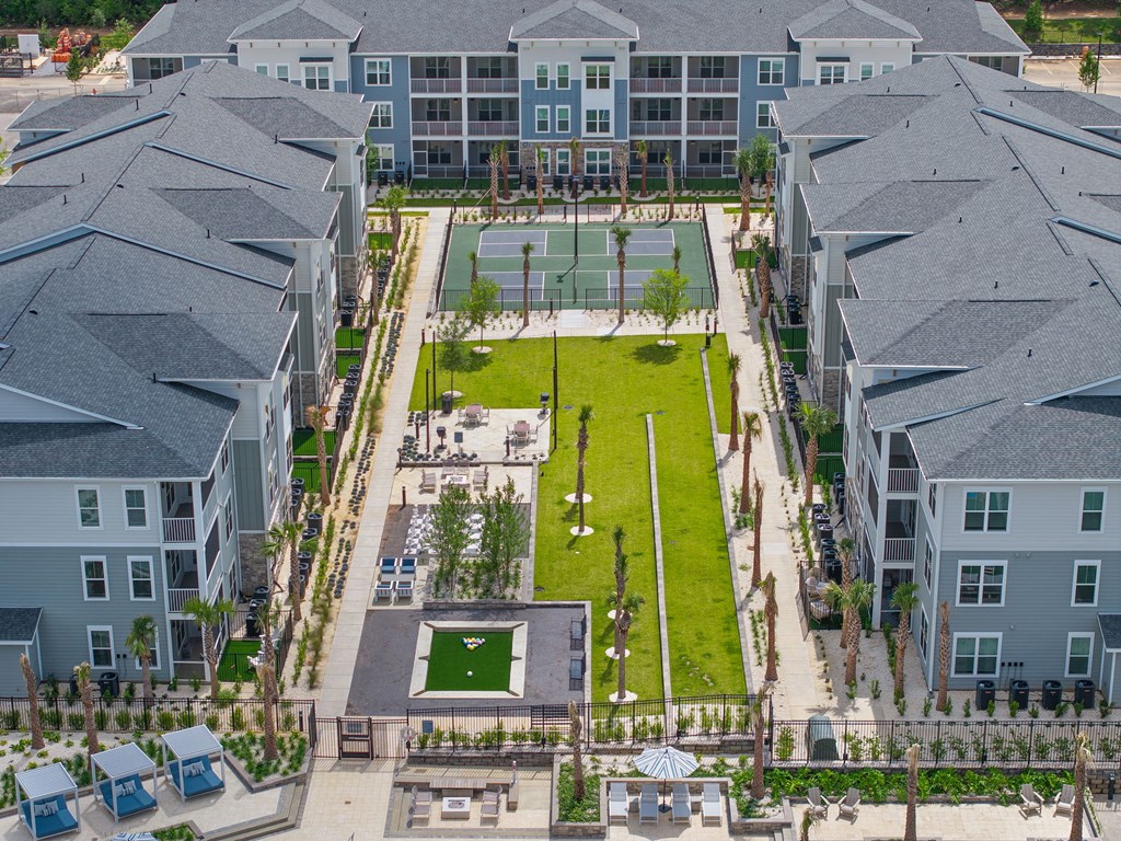 A large grassy area surrounded by buildings with a tennis court in the middle.