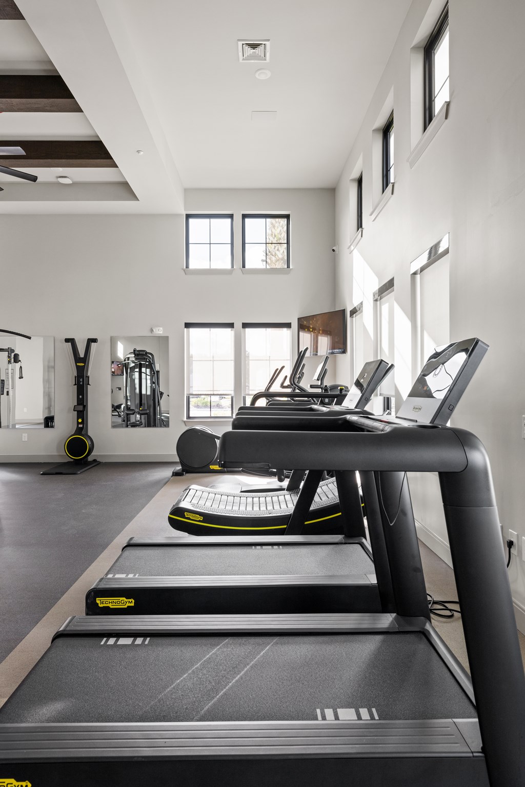 A treadmill in a well lit room with a mirror on the wall.