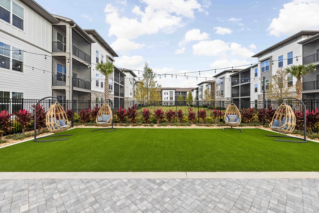 A well-maintained lawn area with swing chairs and apartment buildings in the background.