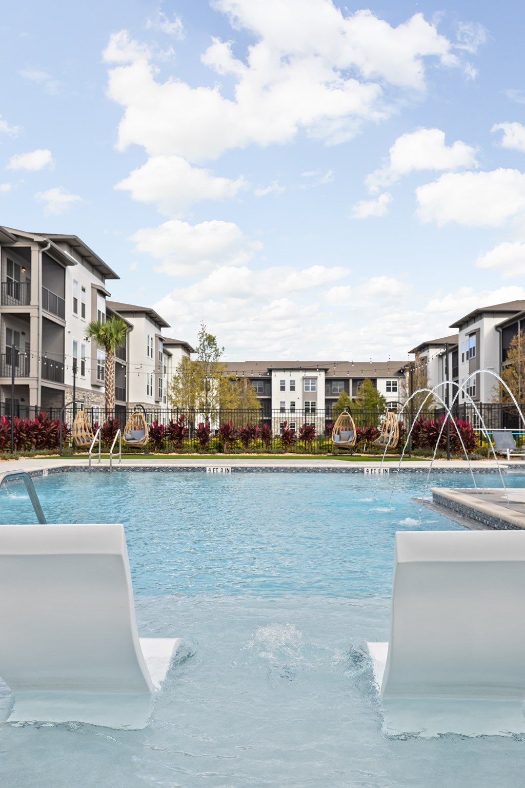 Two white chairs are in the foreground of a swimming pool.
