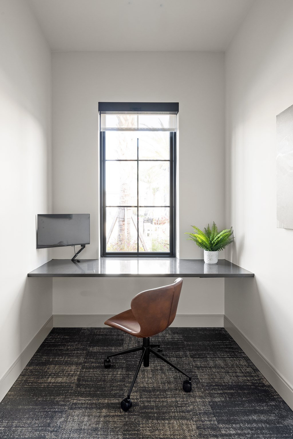 A brown chair is in front of a desk with a monitor and a plant on it.