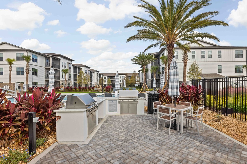 A patio with a table and chairs is surrounded by a black fence and palm trees.
