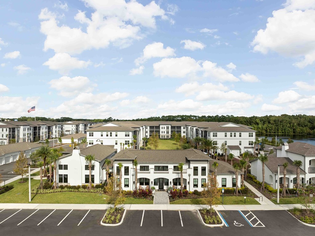 A large white building with a flag on top is surrounded by a parking lot.