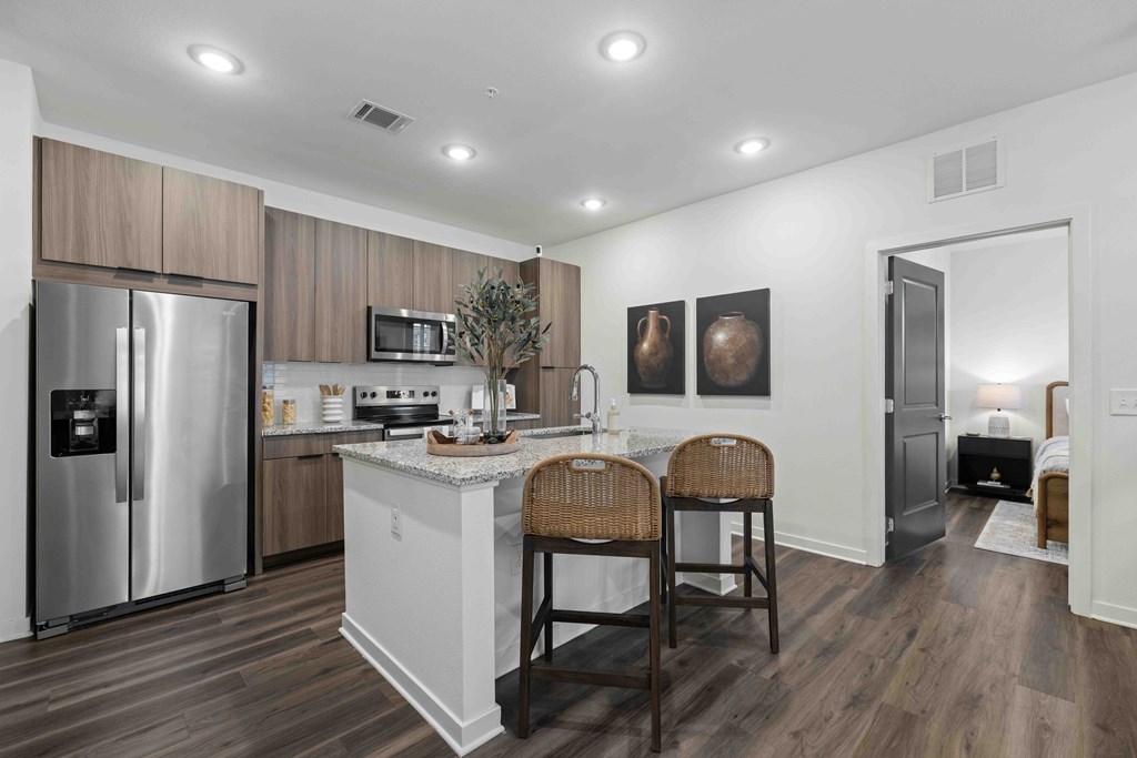 A kitchen with a refrigerator, microwave, and a counter with two chairs.