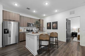 A kitchen with a refrigerator, microwave, and a counter with two chairs.