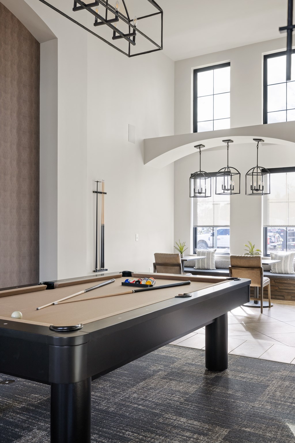 A pool table is in the middle of a room with a high ceiling and a lot of windows.