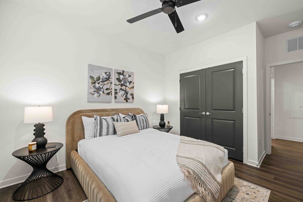 A bedroom with a bed, a ceiling fan, and a side table with a lamp.