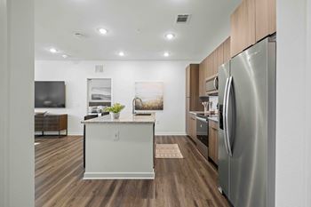 A modern kitchen with a stainless steel refrigerator and wooden flooring.