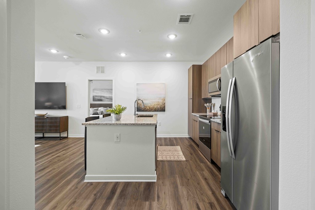 A modern kitchen with a stainless steel refrigerator and wooden flooring.