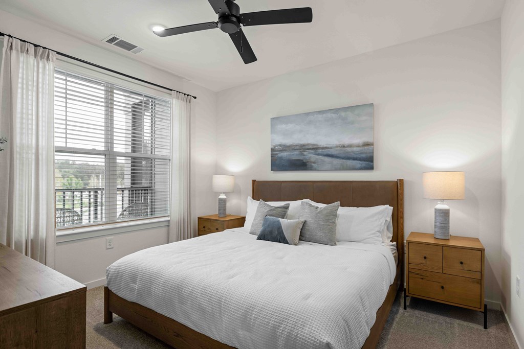 A bedroom with a large bed, a ceiling fan, and a painting on the wall.