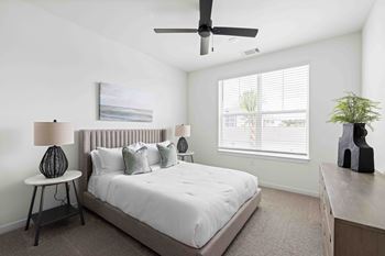 A bedroom with a bed, a ceiling fan, and a painting on the wall.