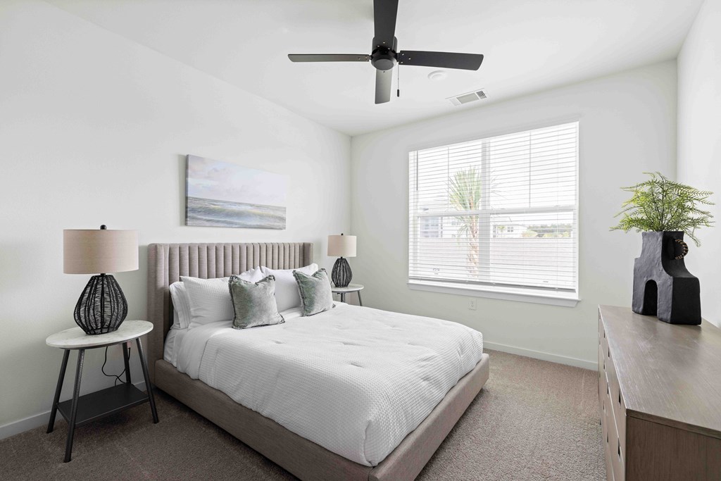 A bedroom with a bed, a ceiling fan, and a painting on the wall.